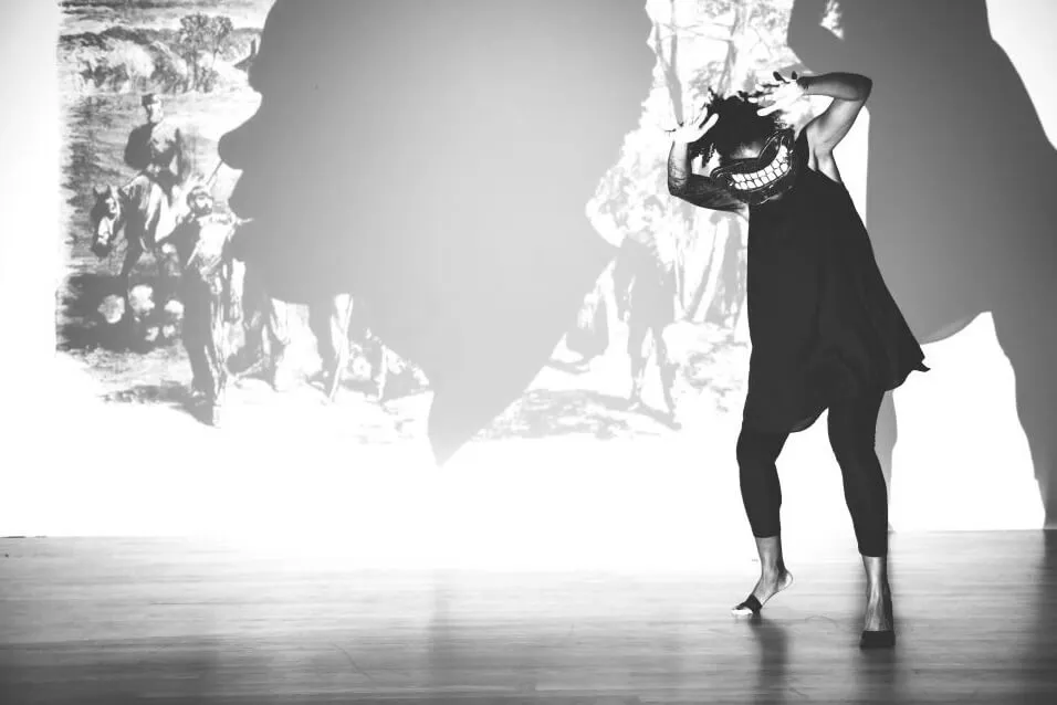 Black and white image a dancer wearing a mask in a dark outfit