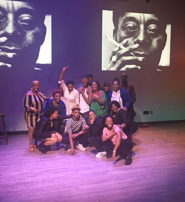 The cast of They Do Not Know Harlem: In Communion with James Baldwin pose for a photo with a picture of James Baldwin behind them.